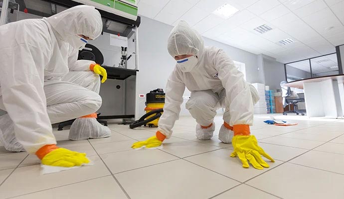 Two professional with full hazmat suits kneeling on a tiled floor to perform sanitization