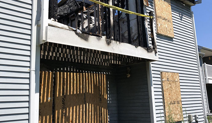 The fire-damaged and boarded-up exterior of an apartment building.