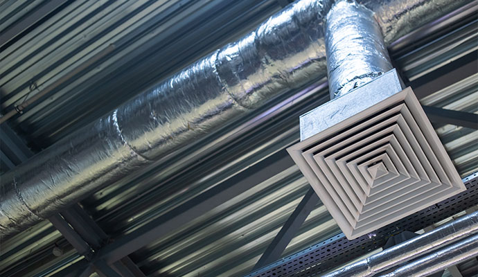 Exposed HVAC ductwork and an air diffuser on a commercial ceiling.