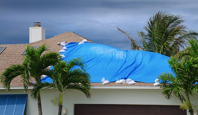 A damaged residential roof covered with blue tarp