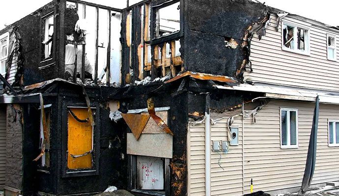 Burned residential property exterior with smoke stains and debris around.