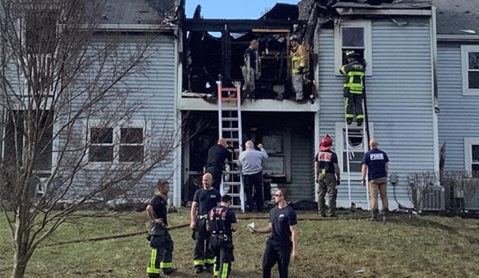 Firefighters responding to a house fire with visible damage to the upper floor