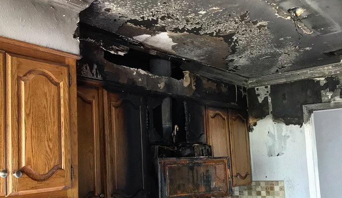 Kitchen interior showing extensive fire damage with a charred ceiling and scorched wooden cabinets