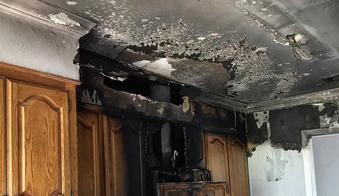 Fire-damaged kitchen showing soot-stained walls, ceiling and cabinets.