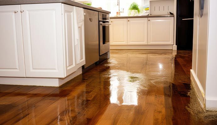 Wooden floor damaged by plumbing leak with visible water on the floor