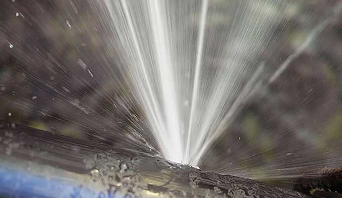 Metal pipe burst with water spraying out forcefully, causing indoor flooding.