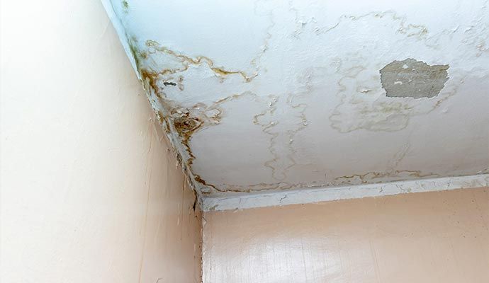 The corner of a ceiling showing water damage with brown stains and peeling paint